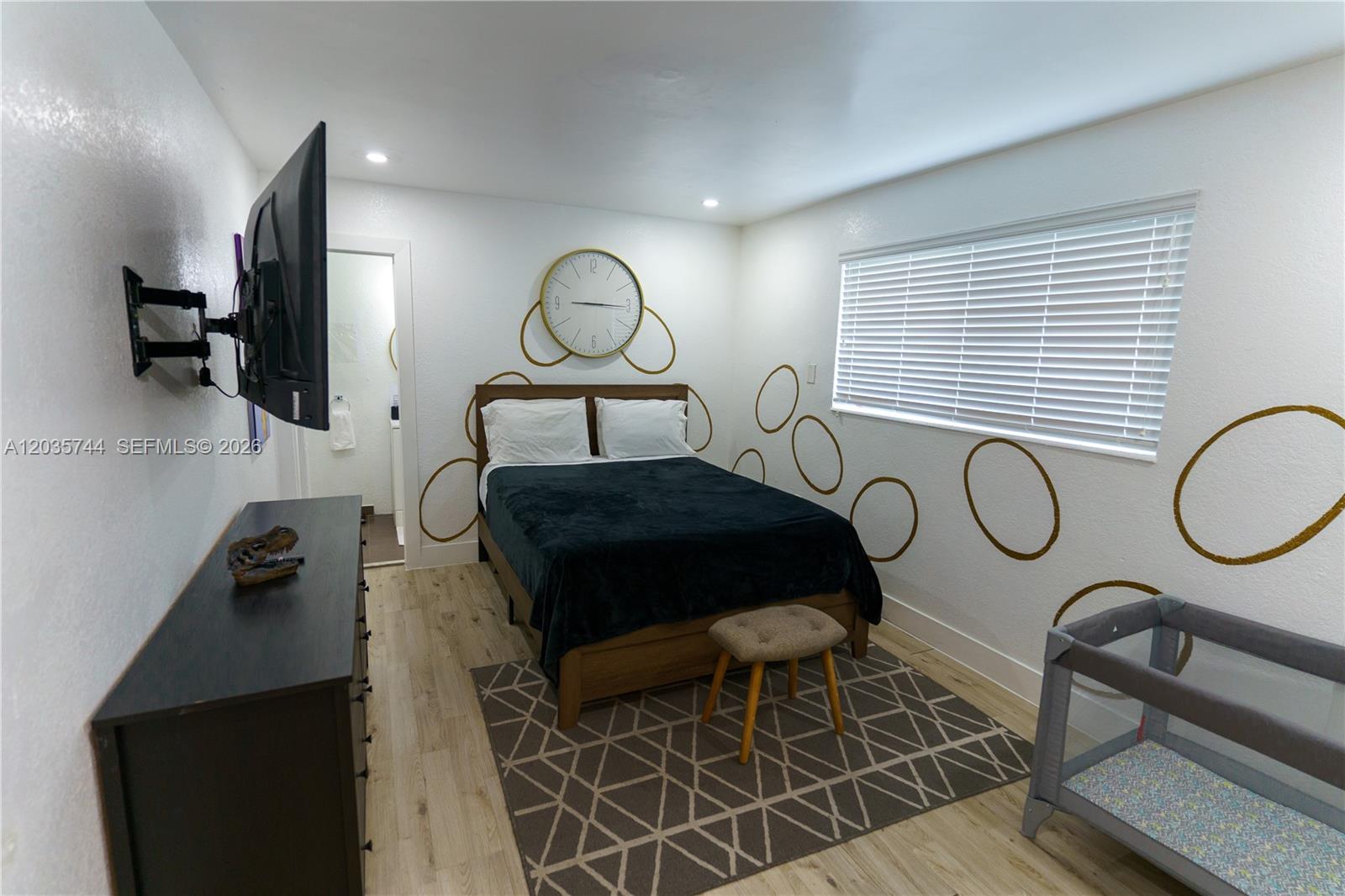 A bedroom features a bed with a dark blanket, a wall clock, and gold circle decals — 310 NE 162nd St, Miami FL 33162, MIAMI, FL