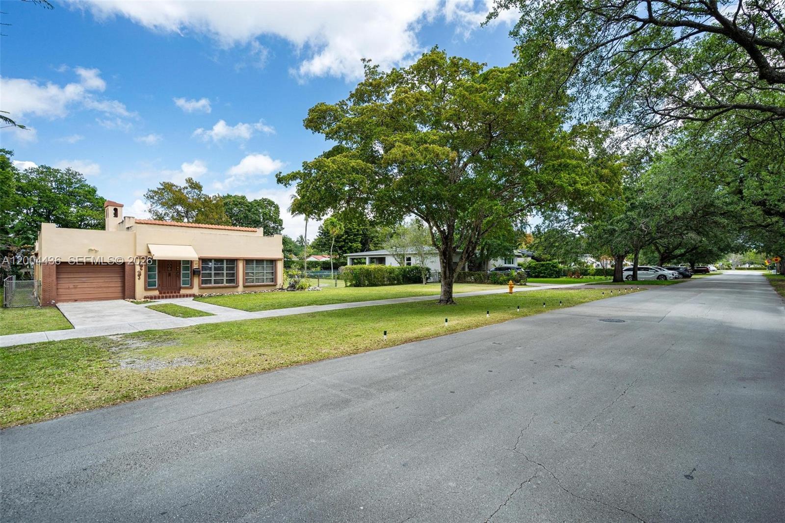 A single-story tan house with a brown garage and a large tree in the yard — 57 N Melrose Dr, Miami Springs FL 33166, MIAMI SPRINGS, FL