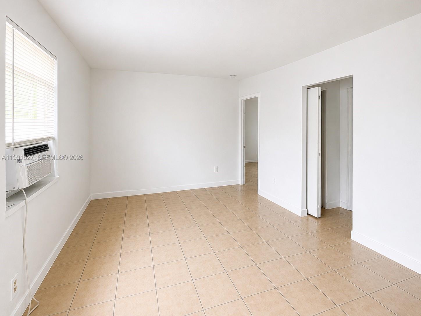 An empty room features white walls, beige tile flooring, a window air conditioner, and two doorways — 2047 Lincoln Ave # 4, Opa-Locka FL 33054, OPA-LOCKA, FL