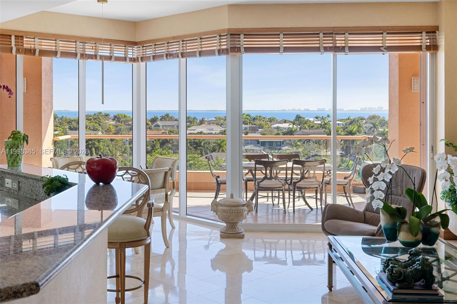 A bright living area with marble floors, a kitchen island, and a balcony overlooking water — 10 Edgewater Dr # 7G, Coral Gables FL 33133, CORAL GABLES, FL