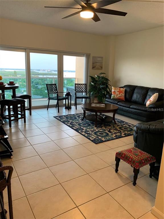 A living room features tile flooring, a black leather sofa, and a balcony with water views — 880 MANDALAY AVENUE UNIT N904, CLEARWATER, FL