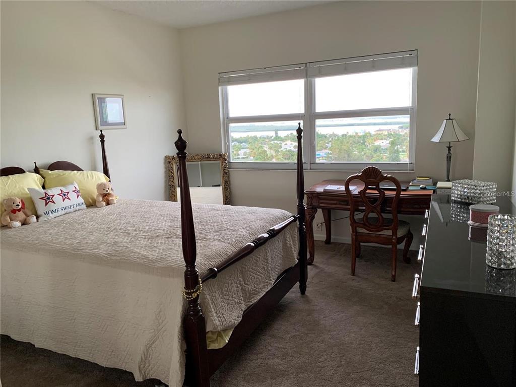 A bedroom features a four-poster bed, a wooden desk, and a window with a water view — 880 MANDALAY AVENUE UNIT N904, CLEARWATER, FL