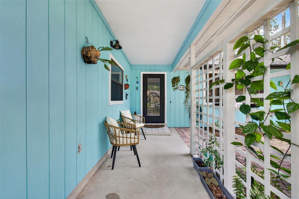 A covered porch features light blue vertical siding, two wicker chairs, and a white trellis — 2518 NW 51ST PLACE, GAINESVILLE, FL