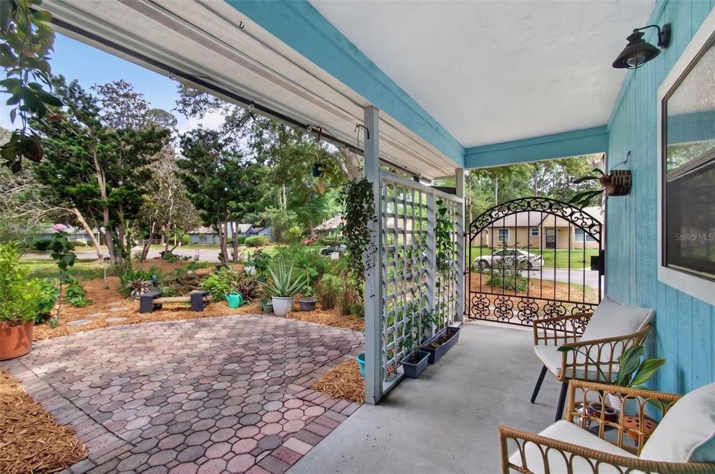 A covered porch with wicker chairs overlooks a brick patio and a landscaped front yard — 2518 NW 51ST PLACE, GAINESVILLE, FL