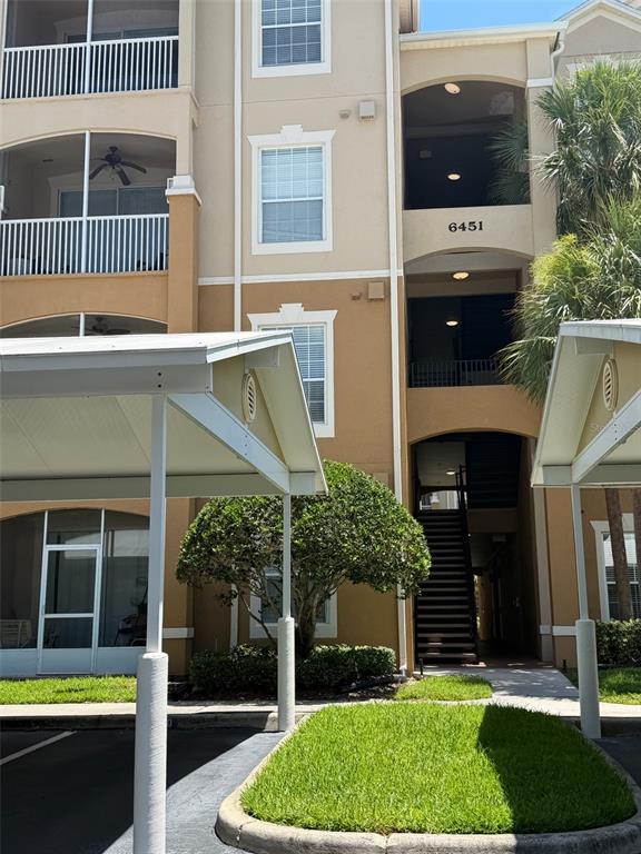 A multi-story apartment building exterior features tan stucco walls, screened balconies, and covered parking spaces — 6451 OLD PARK LANE UNIT 102, ORLANDO, FL