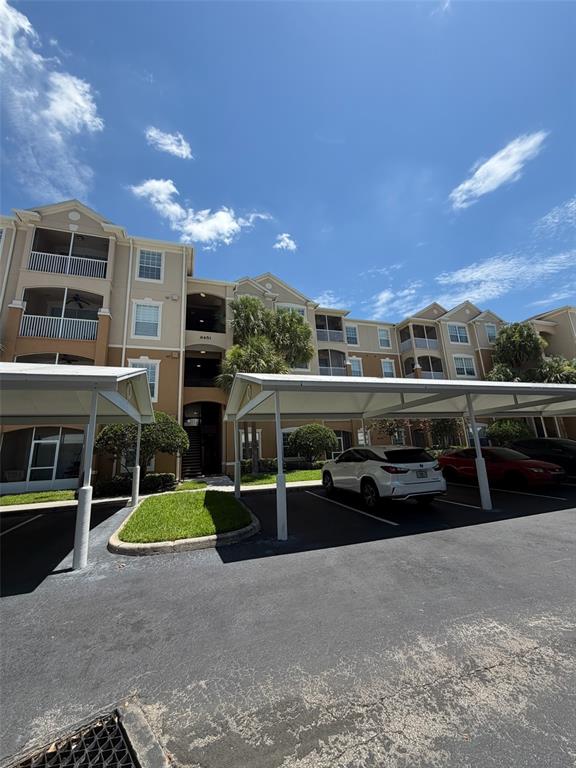 The exterior of a multi-story apartment building features covered parking spaces and a landscaped lawn — 6451 OLD PARK LANE UNIT 102, ORLANDO, FL