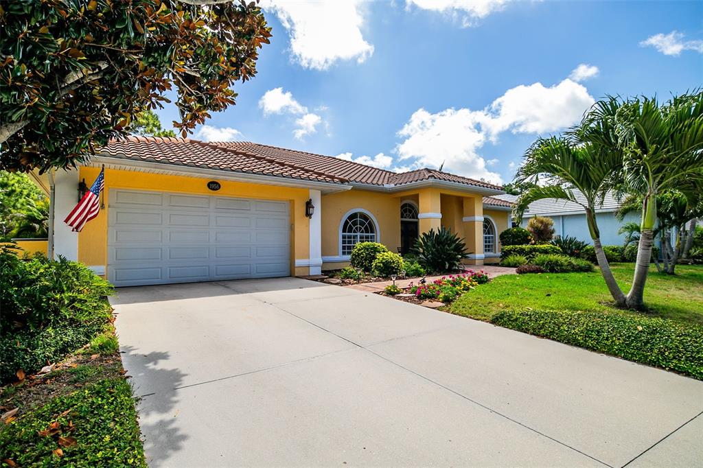 A yellow single-story house with a two-car garage, tile roof, and a concrete driveway — 1956 WHITE FEATHER LANE, NOKOMIS, FL