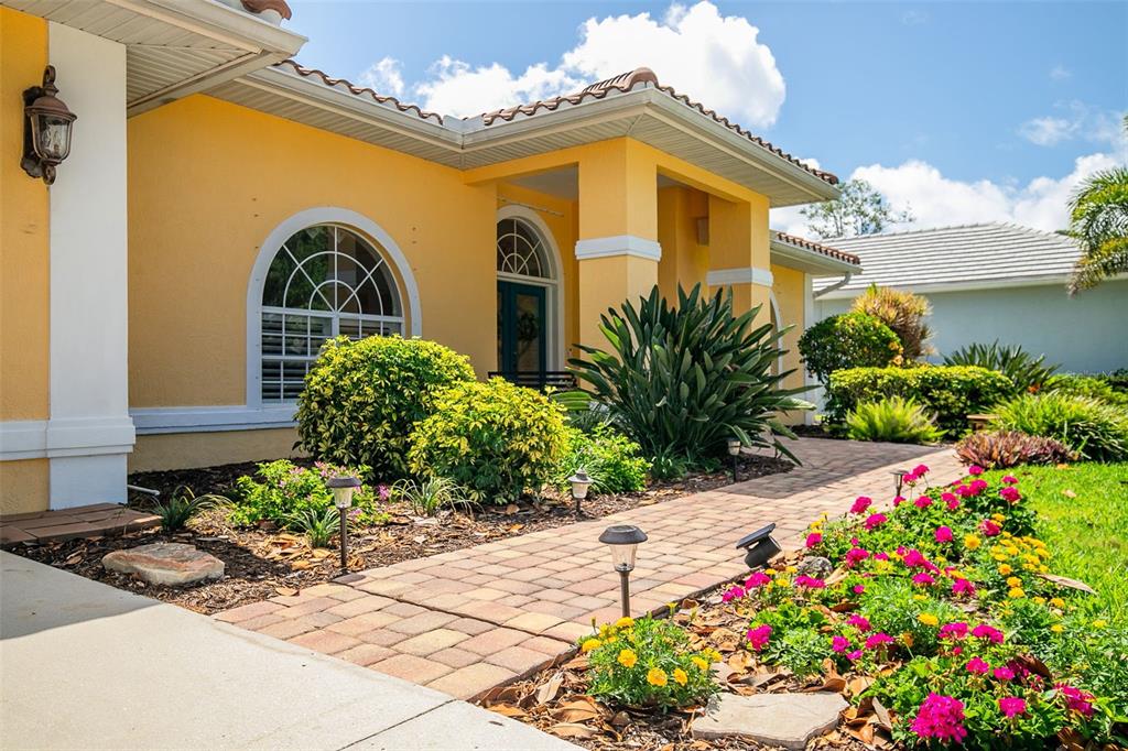 A yellow house exterior features a brick walkway, arched windows, and a landscaped front yard — 1956 WHITE FEATHER LANE, NOKOMIS, FL