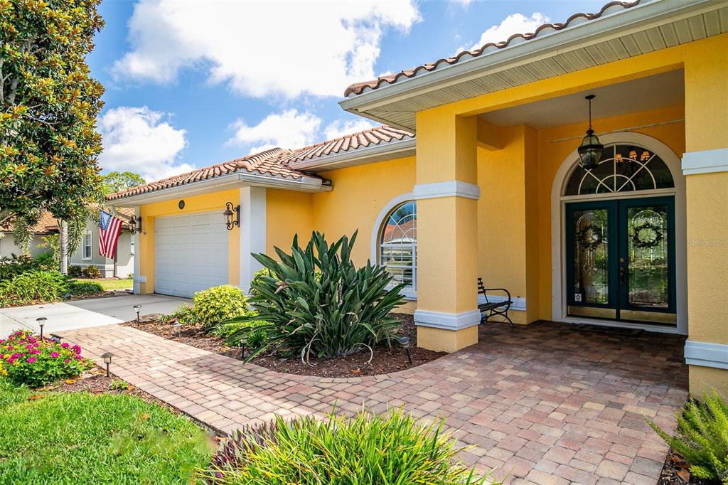 A yellow house exterior features a paved walkway, a double front door, and a garage — 1956 WHITE FEATHER LANE, NOKOMIS, FL