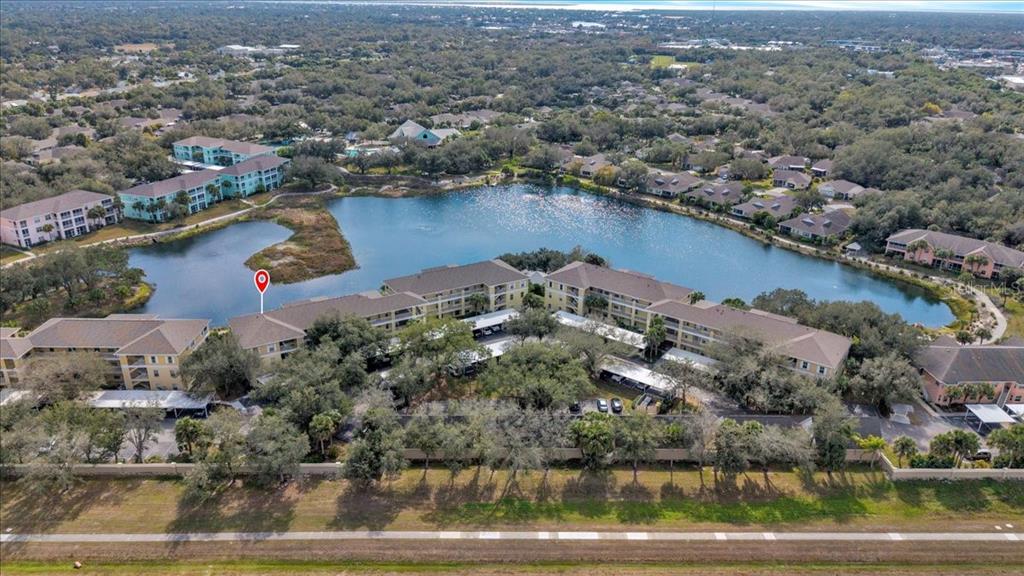 An aerial view shows apartment buildings situated around a lake in a wooded area — 19335 WATER OAK DRIVE UNIT 301, PORT CHARLOTTE, FL