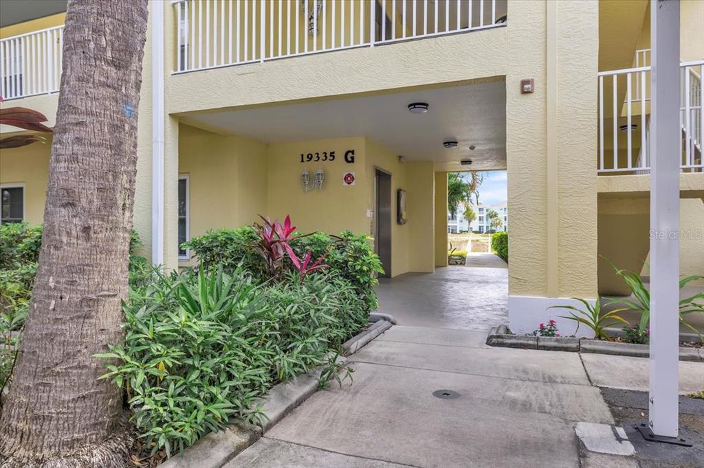 A ground-level view of a yellow apartment building entrance with a walkway and landscaping — 19335 WATER OAK DRIVE UNIT 301, PORT CHARLOTTE, FL