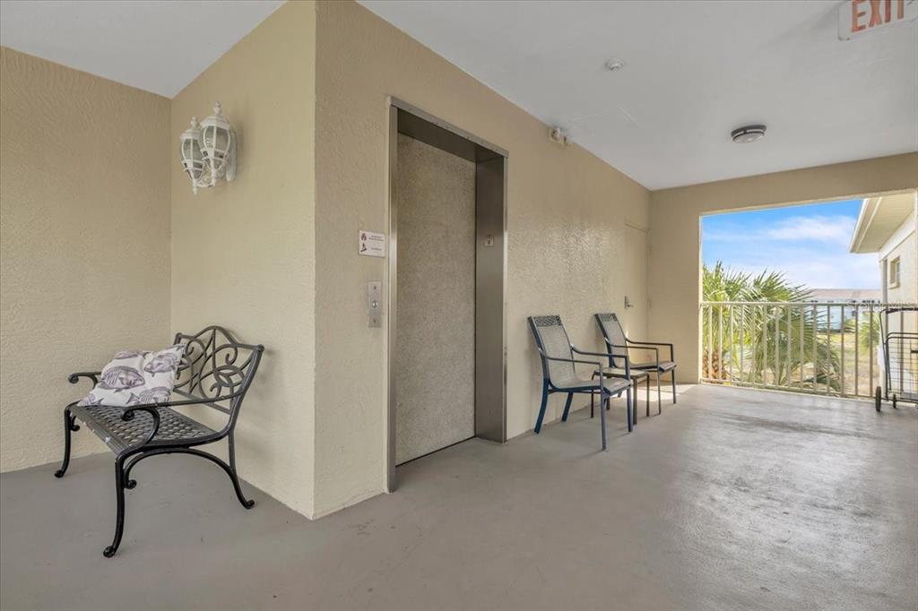 An outdoor elevator landing features a metal bench, two chairs, and a railing overlooking greenery — 19335 WATER OAK DRIVE UNIT 301, PORT CHARLOTTE, FL