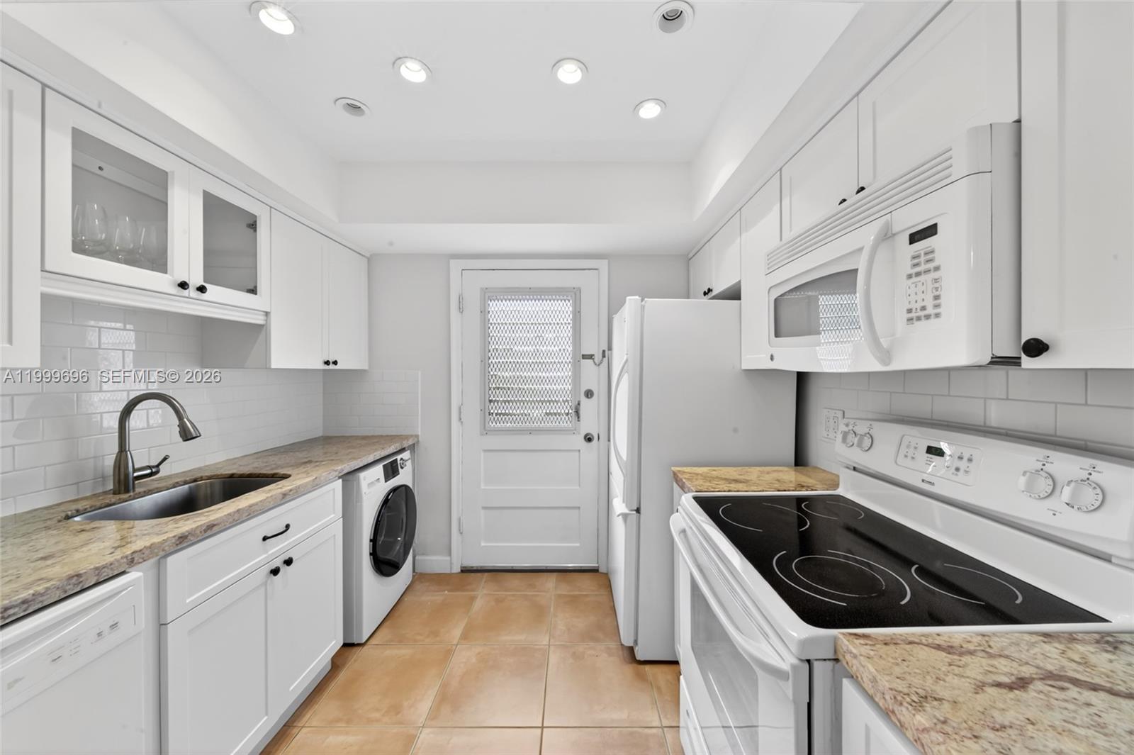 A white kitchen features a built-in washer, granite countertops, and a glass-paneled exterior door — 6815 Edgewater Dr # 108, Coral Gables FL 33133, CORAL GABLES, FL