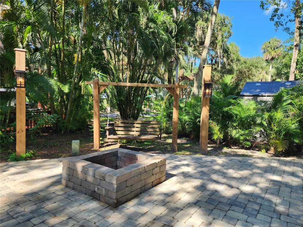 A stone fire pit sits on a paver patio in front of a wooden porch swing — 316 ROAN (GATOR ALLEY) ROAD, RIVER RANCH, FL