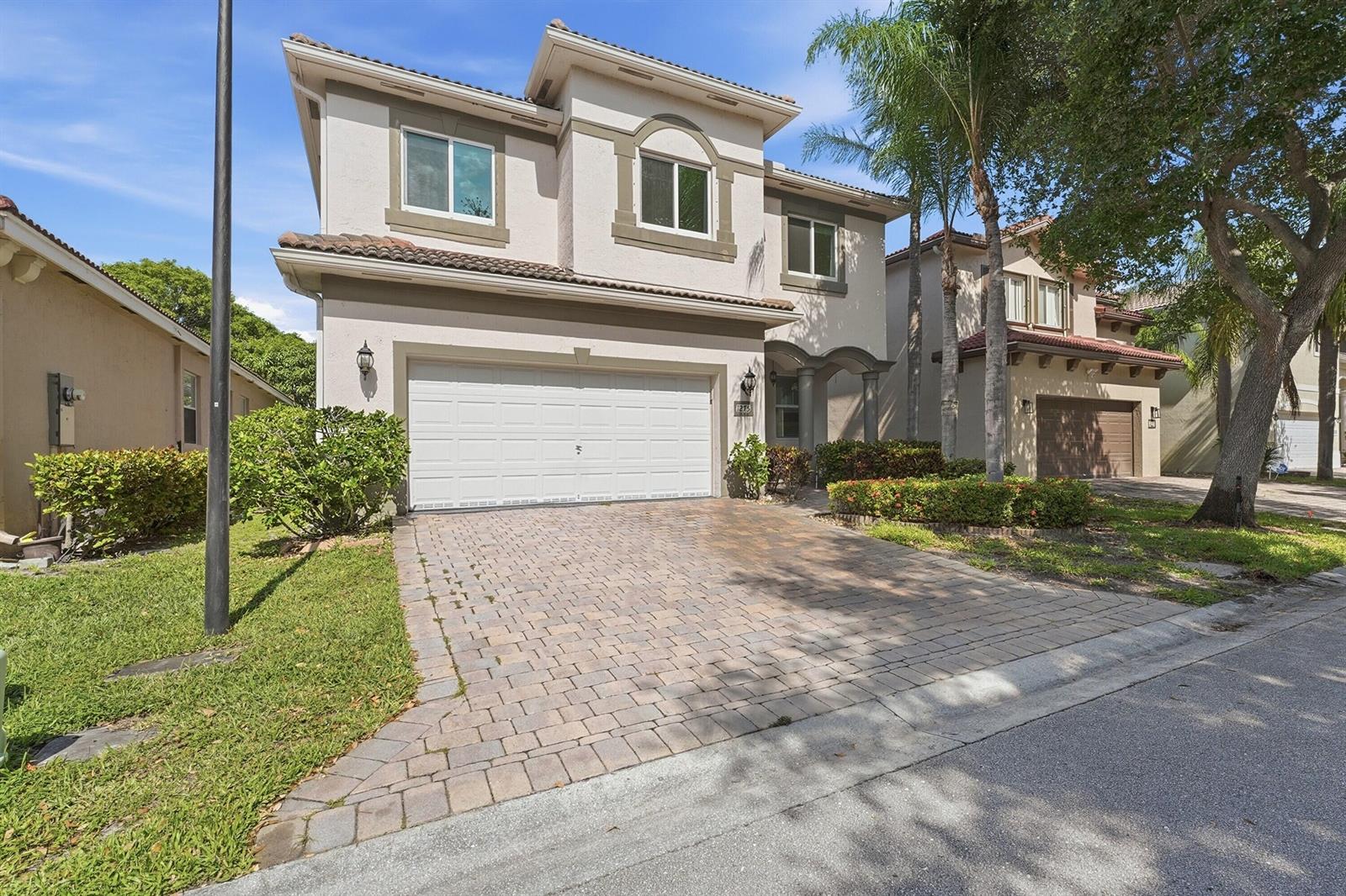 A two-story suburban house with a paved driveway, a two-car garage, and palm trees — 1275 Rosegate Boulevard, Riviera Beach FL 33404, RIVIERA BEACH, FL