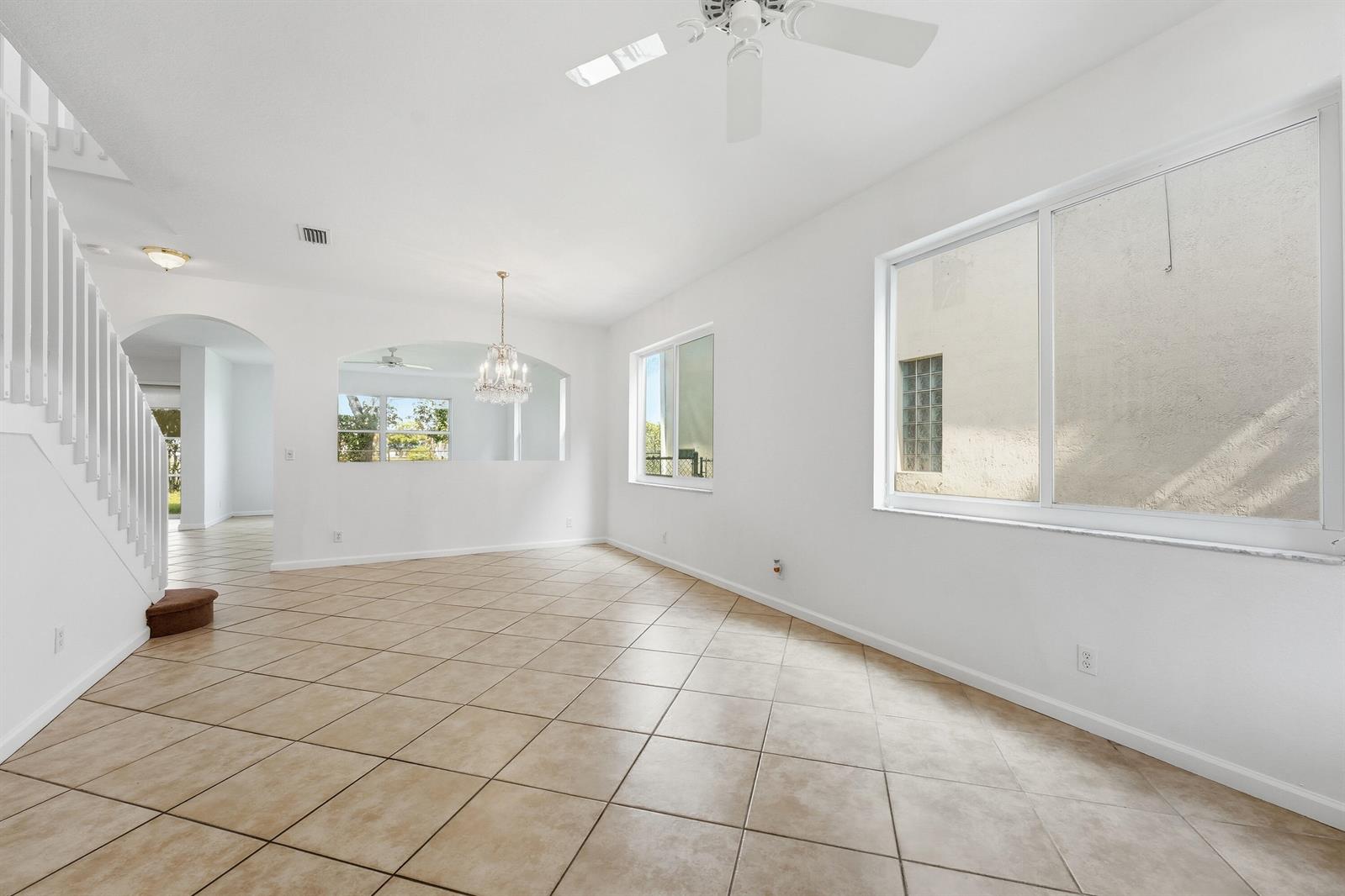 An empty living room features white walls, tile flooring, a ceiling fan, and a staircase — 1275 Rosegate Boulevard, Riviera Beach FL 33404, RIVIERA BEACH, FL