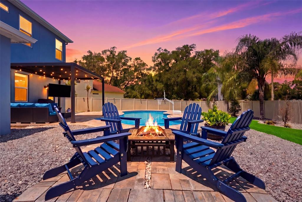 A backyard patio features a fire pit, blue Adirondack chairs, a pool, and a pergola — 10808 WHITLAND GROVE DRIVE, RIVERVIEW, FL