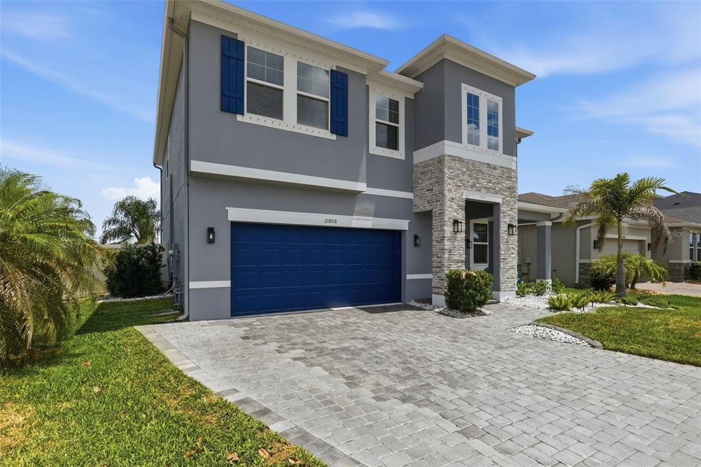 A two-story gray house with a blue garage door and stone facade exterior — 10808 WHITLAND GROVE DRIVE, RIVERVIEW, FL