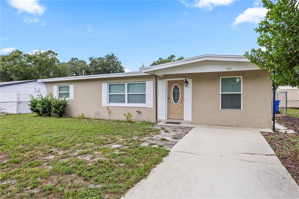 A single-story house with a beige concrete block exterior, a front door, and a concrete driveway — 909 URSULA STREET, OCOEE, FL
