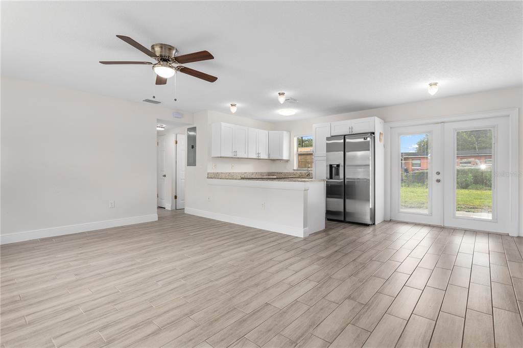 A bright room features light wood-look tile flooring, a ceiling fan, and an open kitchen — 909 URSULA STREET, OCOEE, FL