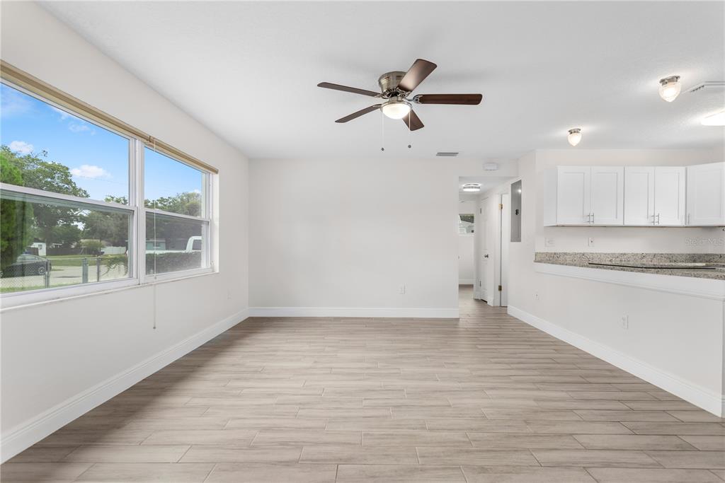 An empty room with light wood-look tile flooring, a ceiling fan, and an adjacent kitchen — 909 URSULA STREET, OCOEE, FL
