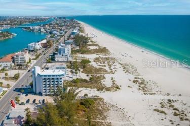An aerial view shows a coastal road, a multi-story building, and a sandy beach — 10200 GULF BOULEVARD, TREASURE ISLAND, FL