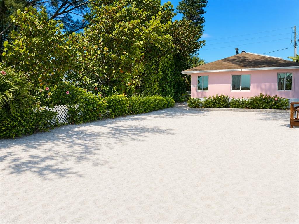 A pink house sits behind a large, sandy yard with lush green landscaping — 10200 GULF BOULEVARD, TREASURE ISLAND, FL