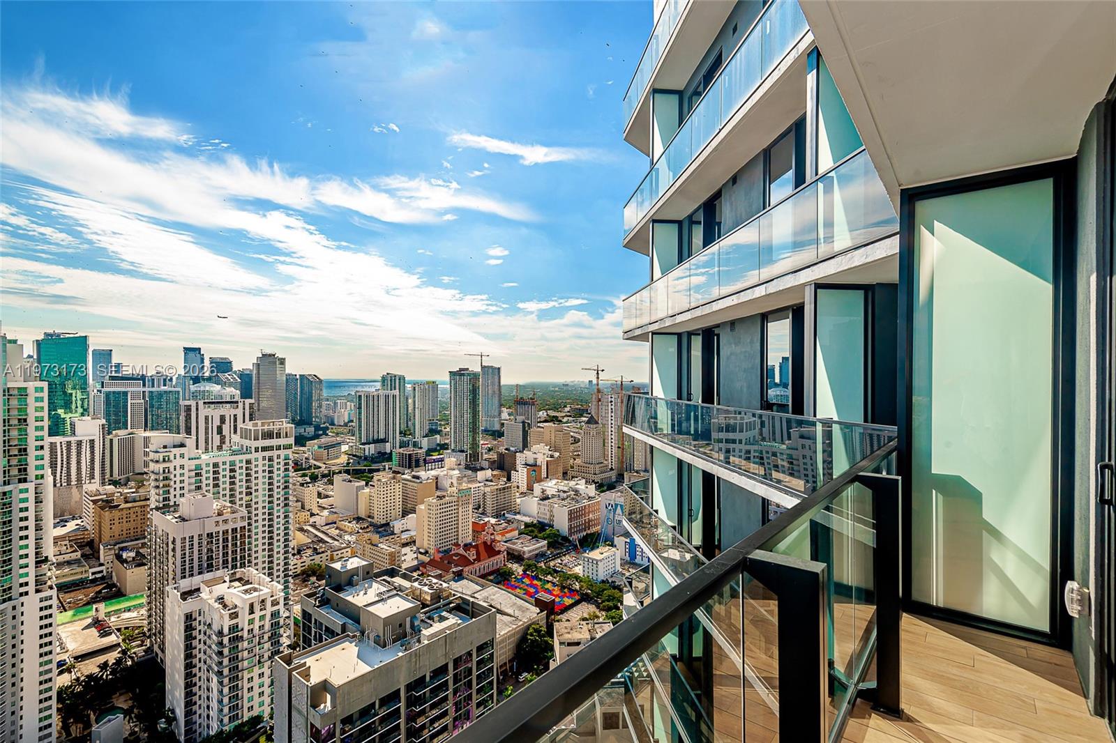 A high-rise balcony with glass railings overlooks a dense urban cityscape under a blue sky — 398 NE 5th St # 4512, Miami FL 33132, MIAMI, FL