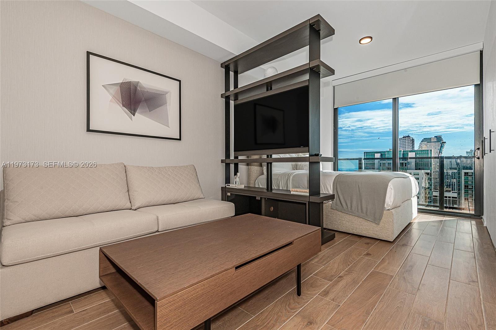 A studio apartment features a sofa, a central shelving unit with a television, and a bed — 398 NE 5th St # 4512, Miami FL 33132, MIAMI, FL