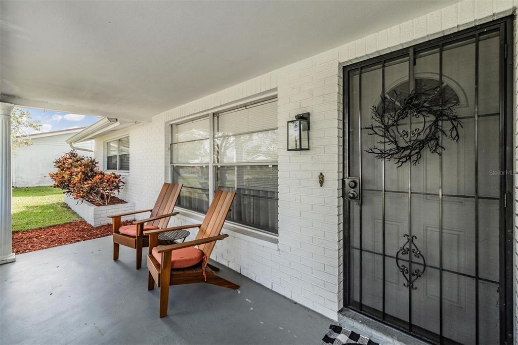 A covered front porch with white brick walls, two wooden chairs, and a security door — 7916 YUCCA DRIVE, NEW PORT RICHEY, FL