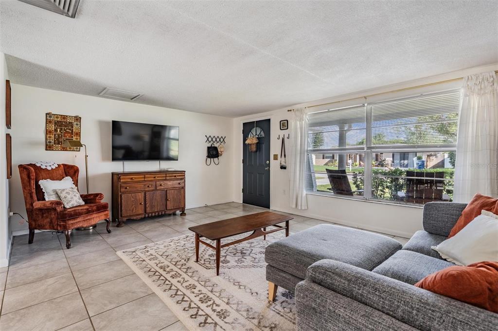 A living room features a gray sectional sofa, a rust-colored armchair, and a wooden console — 7916 YUCCA DRIVE, NEW PORT RICHEY, FL