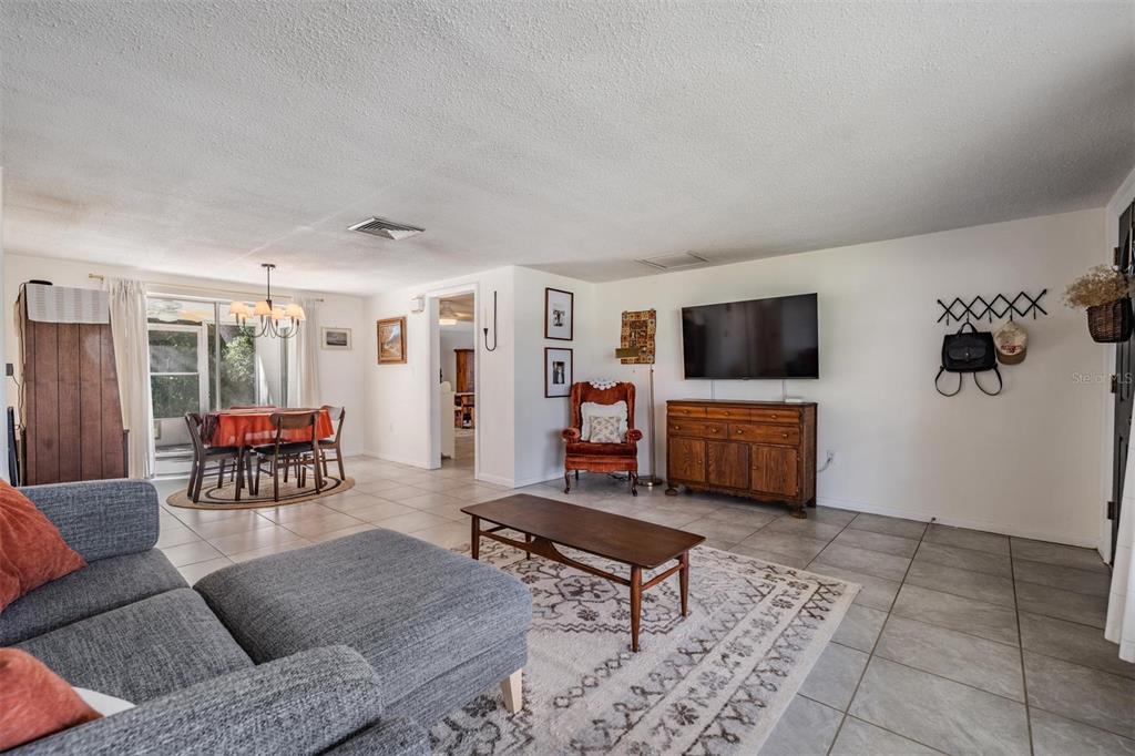 A living room with tile flooring, a gray sectional sofa, a television, and a dining area — 7916 YUCCA DRIVE, NEW PORT RICHEY, FL
