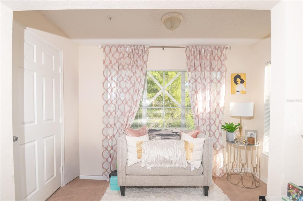 A small seating area features a beige loveseat, patterned curtains, and a round side table — 18001 RICHMOND PLACE DRIVE UNIT 735, TAMPA, FL