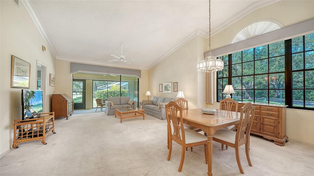 A bright living and dining area with carpeted floors, large windows, and vaulted ceilings — 5456 HAMPSTEAD HEATH UNIT 20, SARASOTA, FL