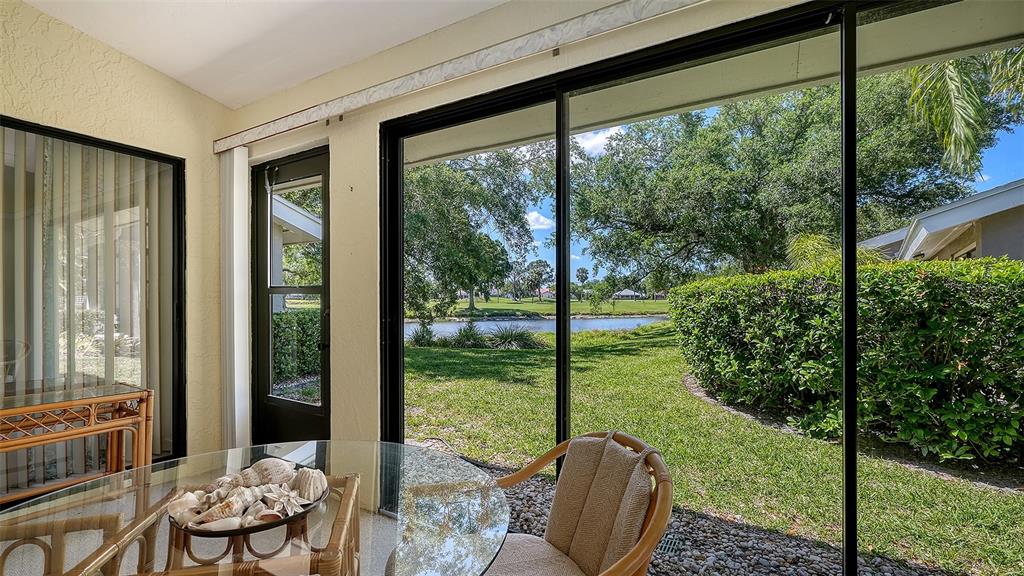 A sunroom features a glass-topped table, wicker chair, and sliding doors overlooking a pond — 5456 HAMPSTEAD HEATH UNIT 20, SARASOTA, FL