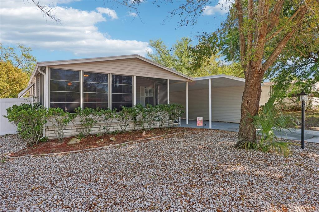 A single-story mobile home with a screened-in porch, carport, and gravel front yard — 39 MAPLEHURST AVENUE, DEBARY, FL