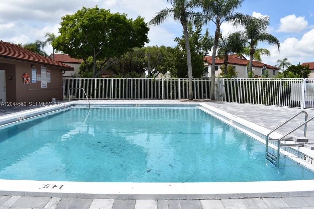 A rectangular swimming pool is surrounded by a paved deck and a white metal fence — PEMBROKE PINES, FL