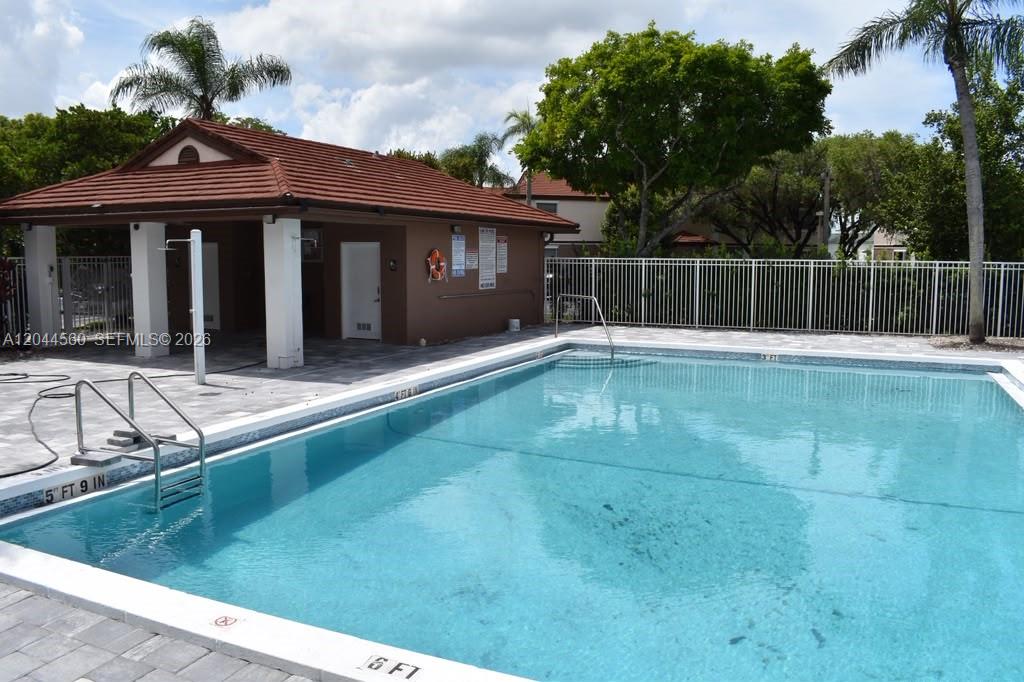 A swimming pool with a depth marker sits in front of a small clubhouse building — PEMBROKE PINES, FL