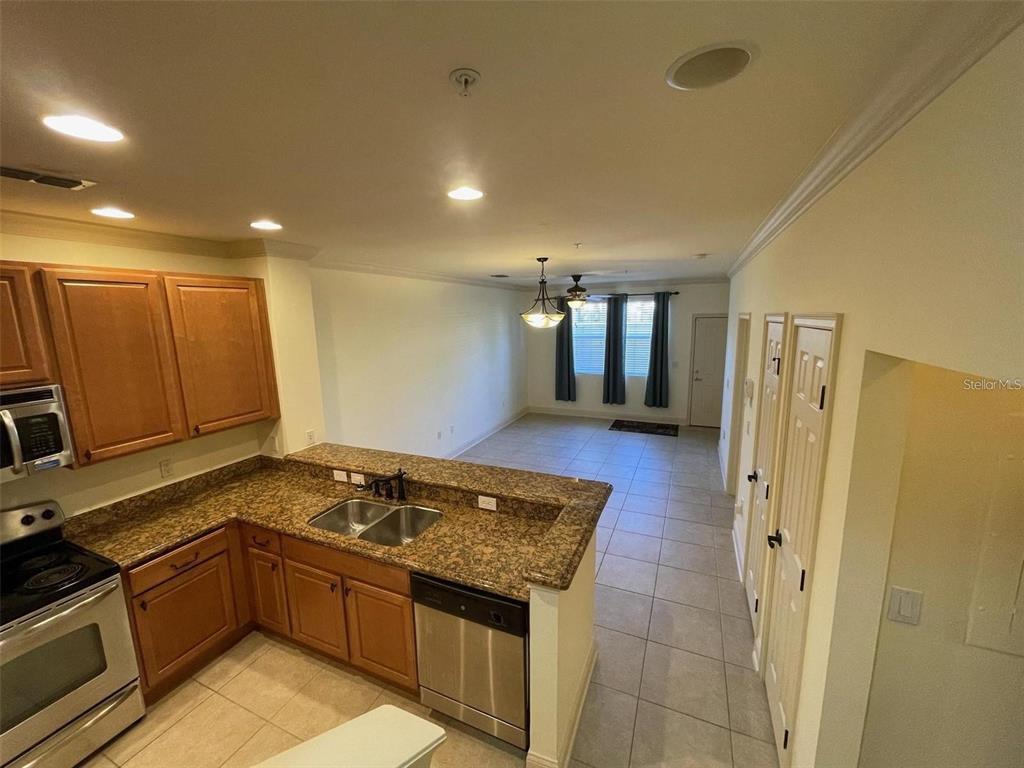 A kitchen with granite countertops and wood cabinets overlooks an open living area — 2846 BELLA VISTA DRIVE, DAVENPORT, FL
