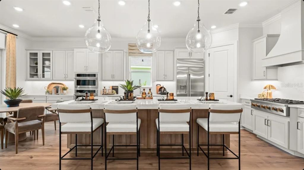 A modern kitchen features white cabinetry, a large central island with bar seating, and pendant lights — 26128 ASPARANO AVENUE, ENGLEWOOD, FL