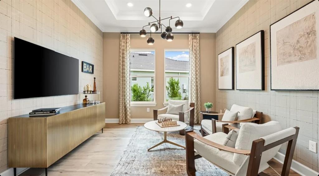 A modern lounge features a gold sideboard, a television, four armchairs, and a central chandelier — 26128 ASPARANO AVENUE, ENGLEWOOD, FL