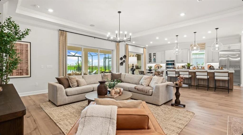 An open-concept living room and kitchen featuring a sectional sofa, island seating, and hardwood floors — 26128 ASPARANO AVENUE, ENGLEWOOD, FL