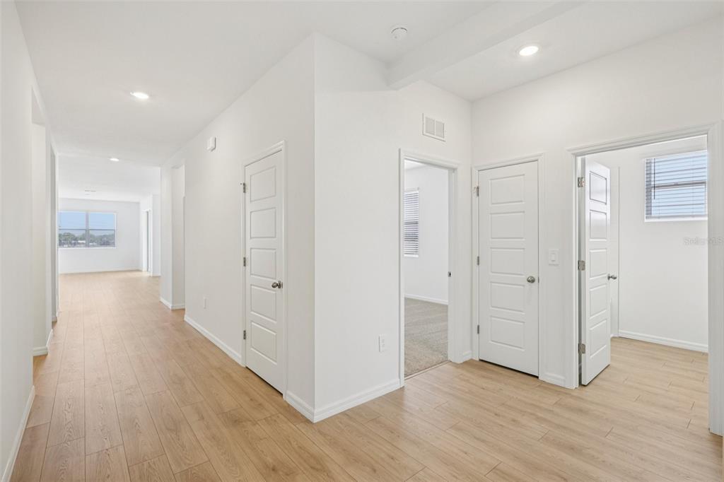 A hallway with light wood-look flooring leads to multiple rooms with white doors and walls — 4665 BARBERRY AVENUE, LAKELAND, FL