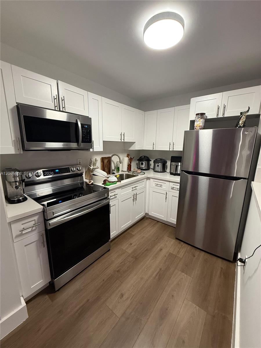 A kitchen features white cabinets, stainless steel appliances, and wood-look flooring — 7155 NW 179th St # 107, Hialeah FL 33015, HIALEAH, FL