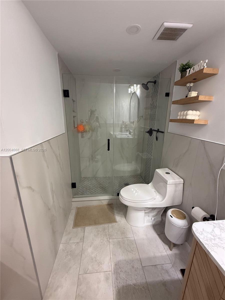 A bathroom features a glass-enclosed shower, a white toilet, and floating wooden shelves — 7155 NW 179th St # 107, Hialeah FL 33015, HIALEAH, FL