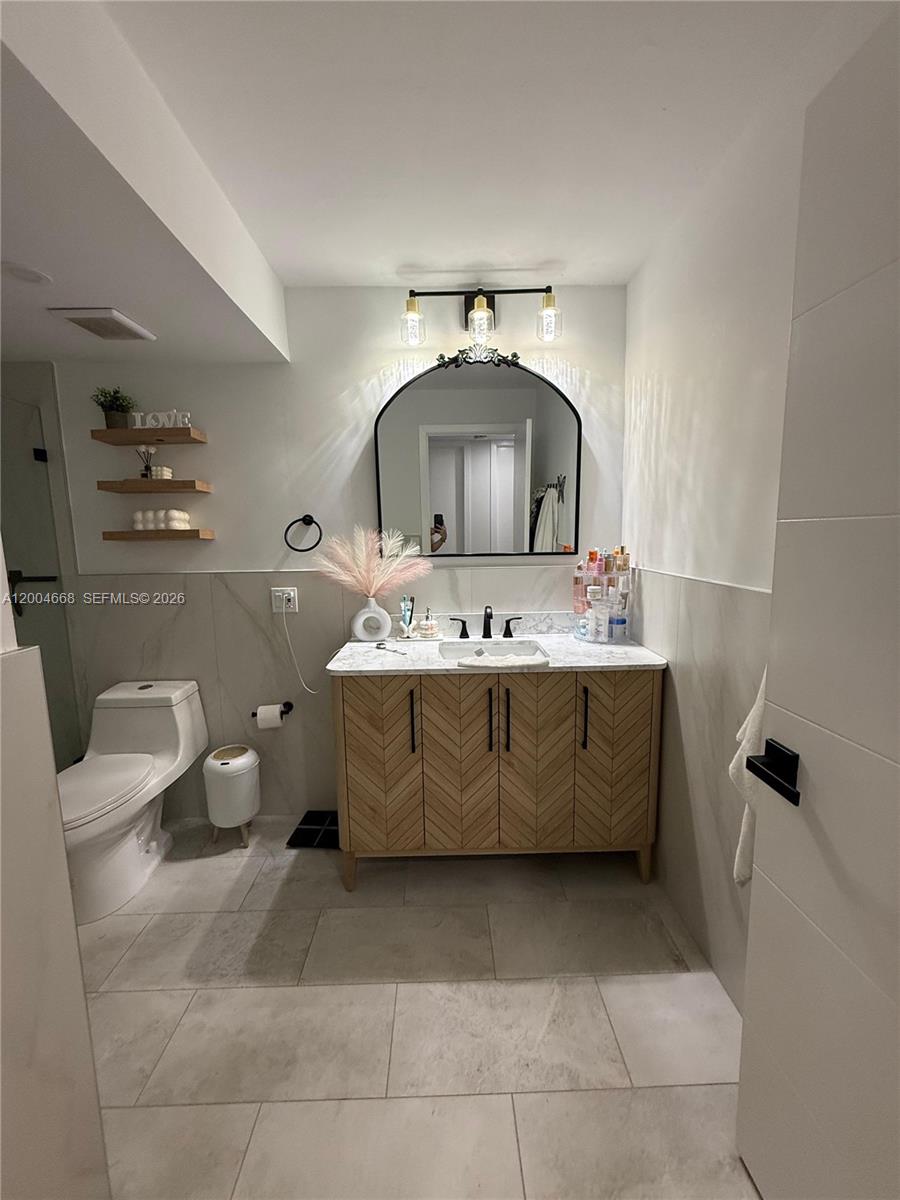 A bathroom features a wooden vanity, an arched mirror, and floating shelves on the wall — 7155 NW 179th St # 107, Hialeah FL 33015, HIALEAH, FL