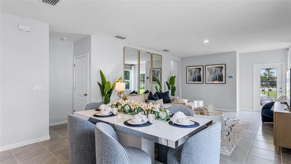 A dining area with a white table and grey chairs opens into a living room — 7182 FLINT CREEK DRIVE, LAND O LAKES, FL