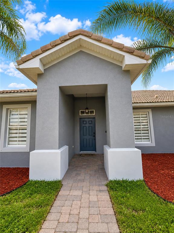 The exterior of a gray house features a covered entryway with a dark blue door — 3402 GREAT POND DRIVE, KISSIMMEE, FL