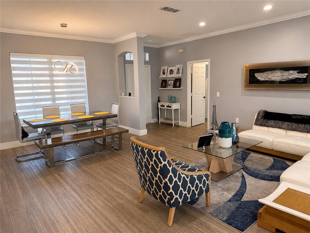 An open-concept living and dining area features light gray walls, wood-look flooring, and modern furniture — 3402 GREAT POND DRIVE, KISSIMMEE, FL