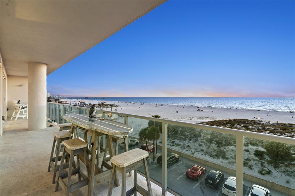 A balcony with a high-top table and stools overlooks a sandy beach and ocean — 15 AVALON STREET UNIT 502, CLEARWATER BEACH, FL